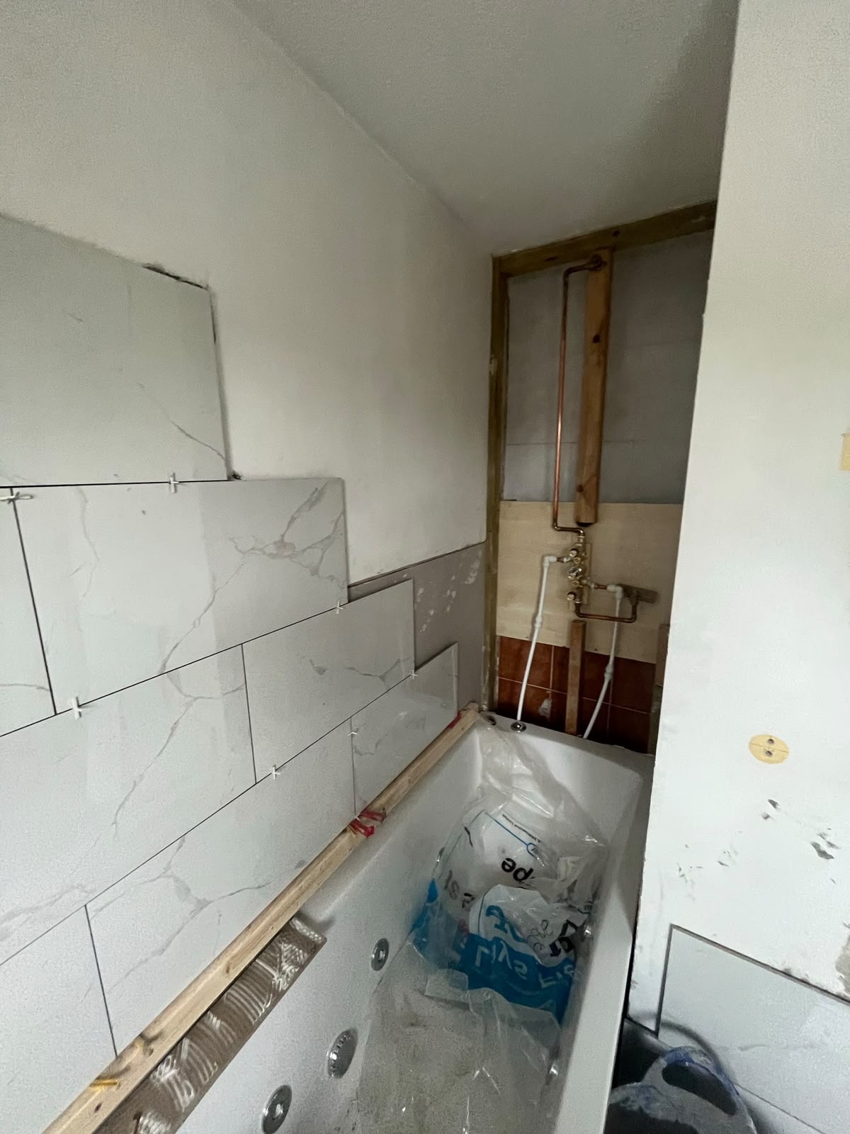 Marble-effect wall tiles being fitted above a bath, RV Renovation, Oxford
